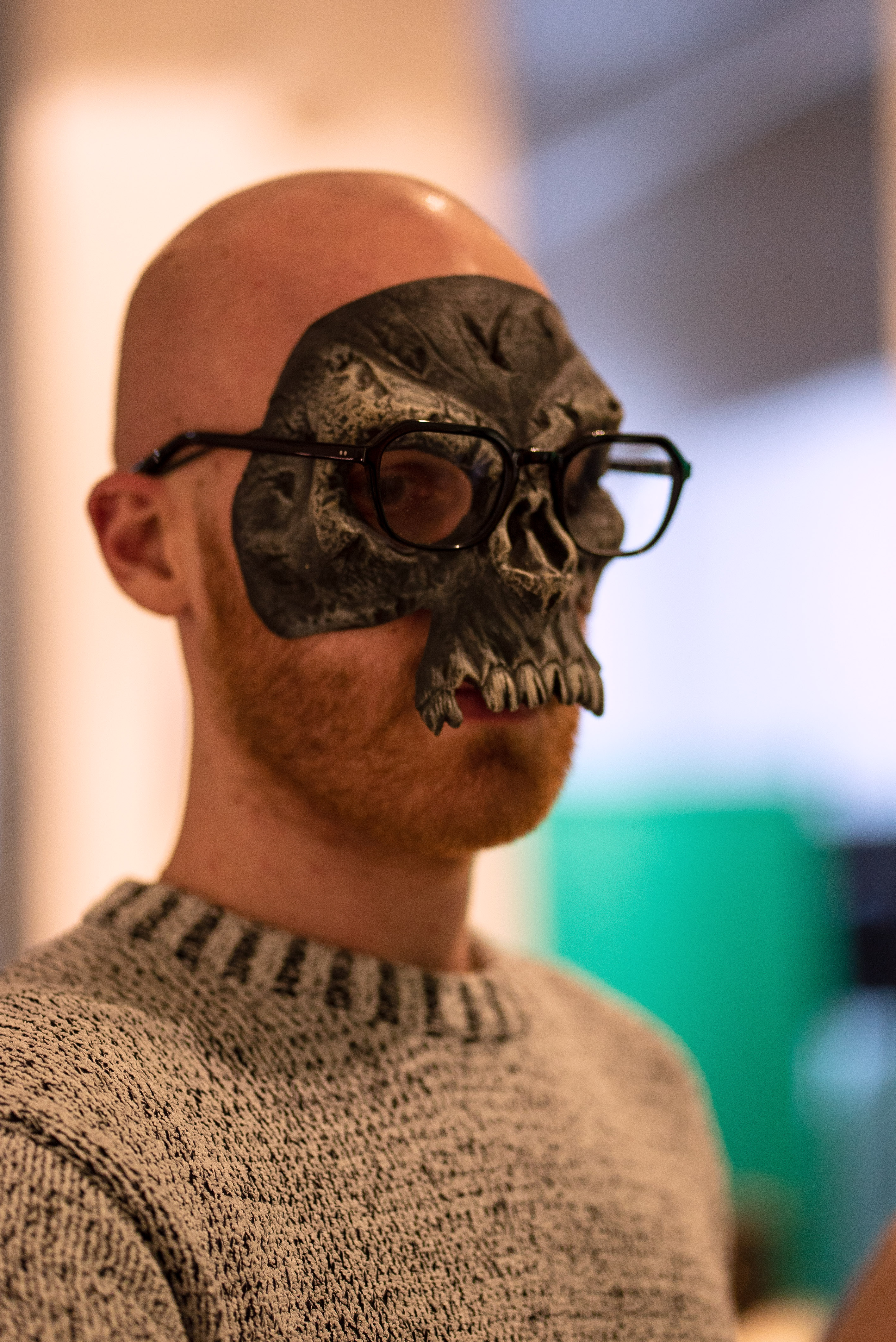 The photo is a close up shot of a person wearing a skull mask. On top of the skull mask they wear their glasses.