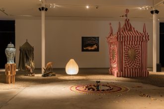 Image of installed art in a gallery space, with a circus tent and other artwork positioned around the space in low lighting