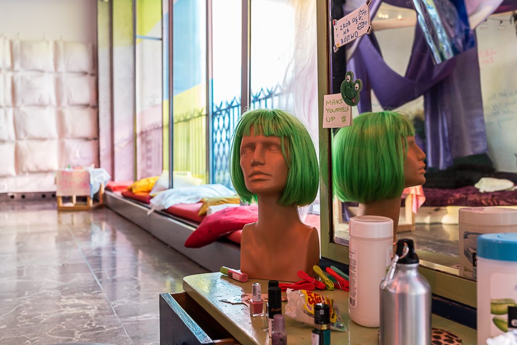 A mannequin head with a green wig, a mirror and makeup.