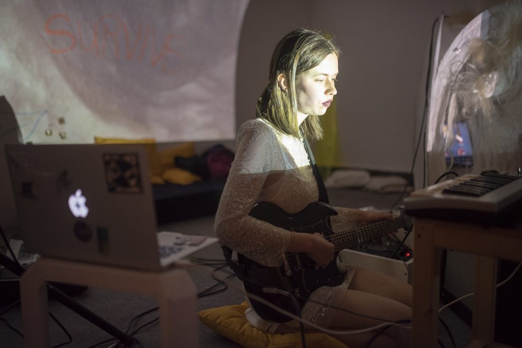 A person sitting in front of a computer with a guitar.