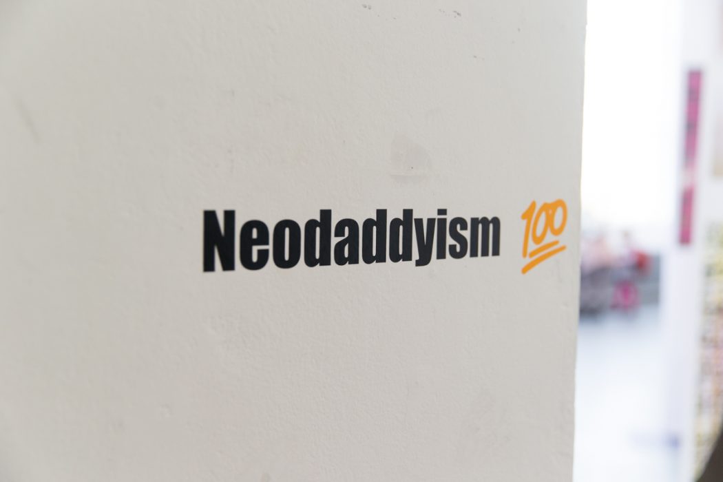 neodaddyism 100 title on white wall, neodaddyism in black text with 100 in orange