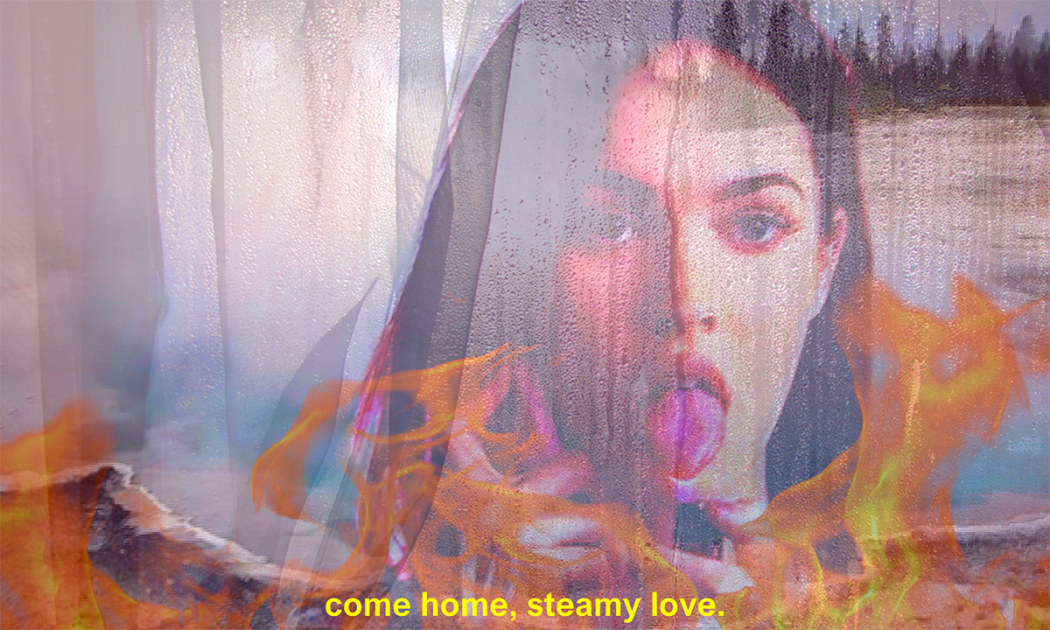 An image of Megan Fox from Jennifer's Body projected on a white curtain, with flames across the bottom of the screen and "come home, steamy love" in yellow text across the bottom.