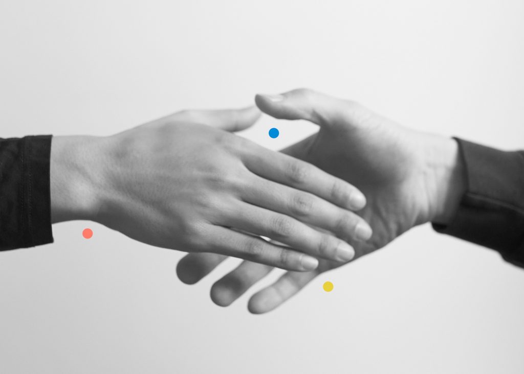 A black and white image of two hands about to touch or shake, presented symmetrically from the wrist down. A red dot is under the wrist, a yellow dot is under the pinky finger, and a blue dot is between the two thumbs in the frame.