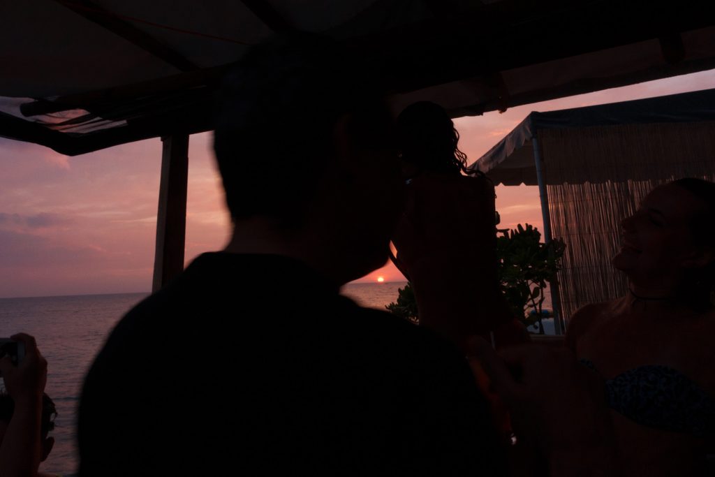 An image of a sunset and an out of focus silhouette of a person and a house.