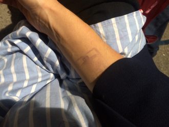 This is a detail shot photo of someone’s wrist, their skin a color like milky coffee, and just barely visible on their inner wrist is a faded stamp, like the kind one may get as they enter a party or club they’ve paid entrance for.