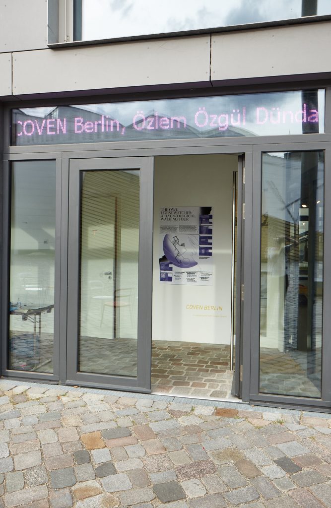 The entrance to feldfünf with COVEN's exhibited work visible through the door, and COVEN BERLIN's name scrolling along an LED banner above the door.