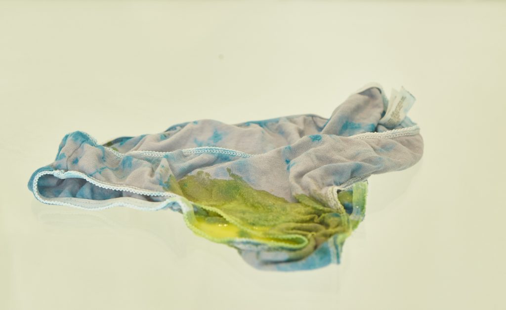 Tie-dyed underwear covered in yellow slime in a glass display case