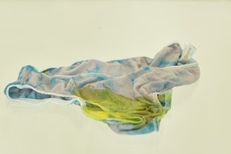 Tie-dyed underwear covered in yellow slime in a glass display case