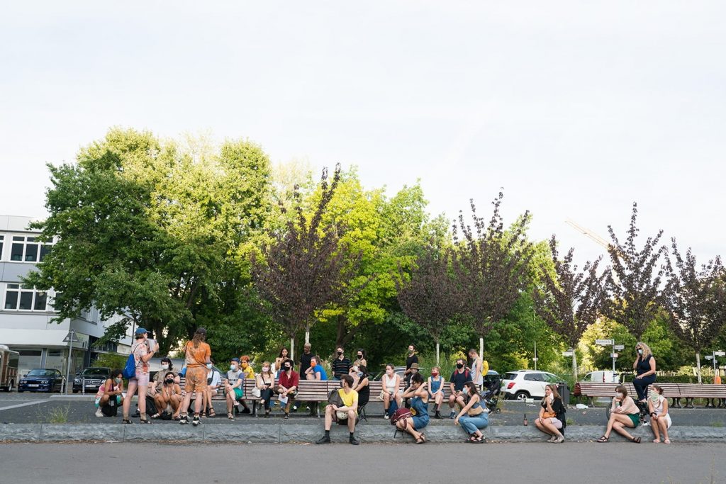 The audience sits in a park promenade watching Frances and Louise.