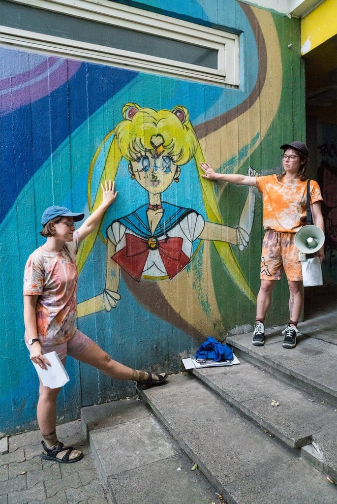 Frances and Louise lovingly put their hands on a mural of Sailor Moon with graffitied satanic symbols on her.