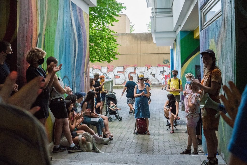 The audience applauds Frances and Louise, in a shaded passageway covered with murals