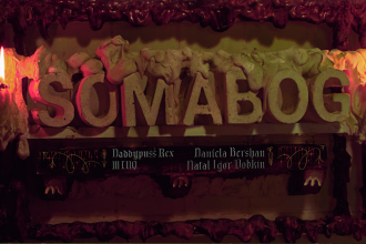 Letters made out of plaster spell out "somabog". Candles are lit next to them, with goopy foam in red and brown. The names Daniela Bershan, Daddypuss Rex, Miq, and Natal Igor Dobkin are written in old-looking script below.