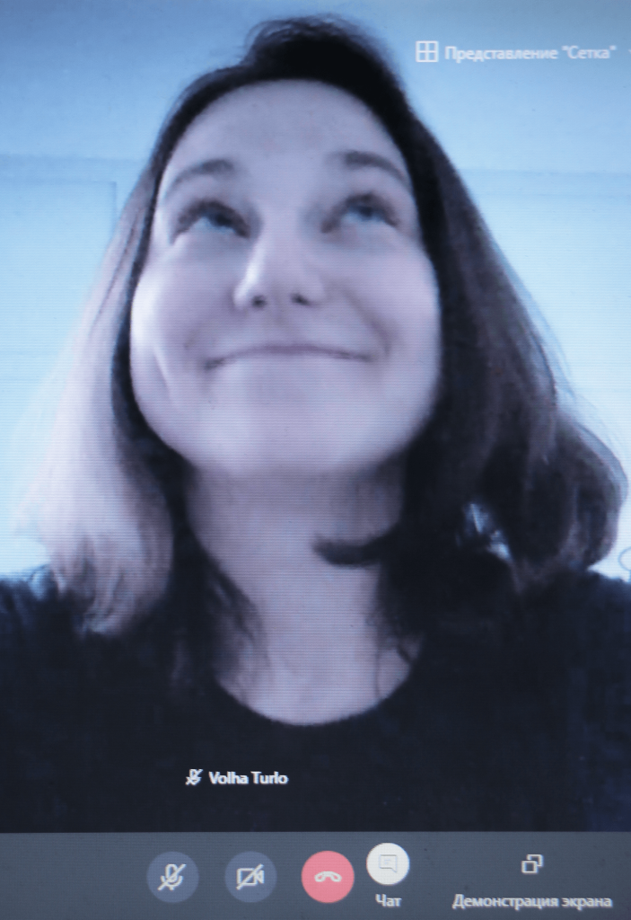 This looks like a screenshot from a zoom call with someone because their name is on view as well as the options to end the call or mute. This person looks like a white woman with dark, shoulder-length hair who is seen slightly from below, and smiling with their mouth closed.