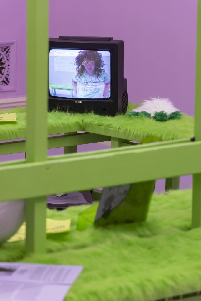 This is the beginning of a series of shots of the TV, which feature a different point in the dance that’s being shown on the TV, which was filmed in this same space. In this shot, the TV is seen from another angle in the space and the dancer is looking down, her long curly brown hair obscuring her face.