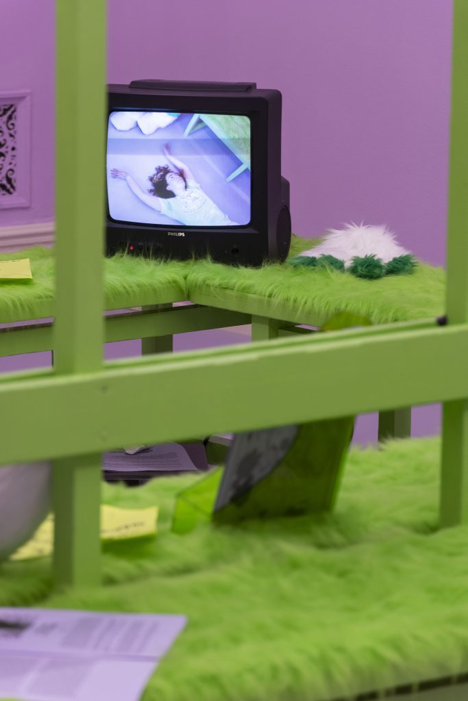 This is the beginning of a series of shots of the TV, which feature a different point in the dance that’s being shown on the TV, which was filmed in this same space. In this shot, the TV is seen from another angle in the space and the dancer is lying down, her long curly hair expanding out around her face.