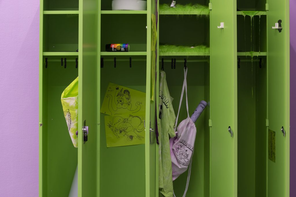This is a shot of just the interior of the lockers, which are bright green. We see that there is slime that has poured down in icicle-like spikes down the shelves inside the lockers. We also see sexy fan art featuring Ariel and Ursula from Disney animated version of The Little Mermaid.
