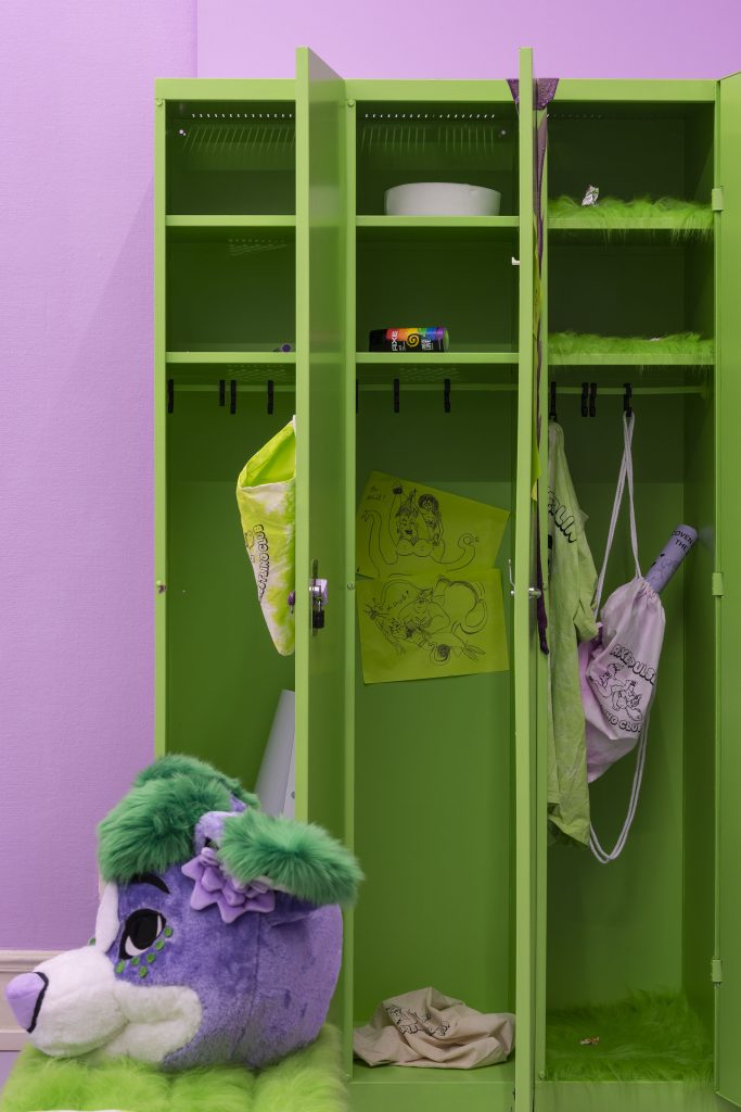 This is a shot of just the interior of the lockers, but from further away, which are bright green. We see that there is slime that has poured down in icicle-like spikes down the shelves inside the lockers. We also see sexy fan art featuring Ariel and Ursula from Disney animated version of The Little Mermaid. We also see the mascot head.