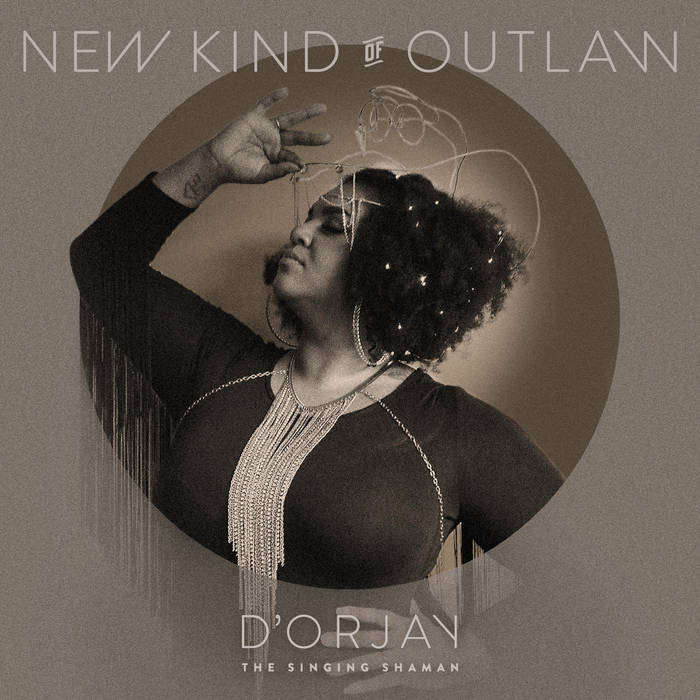 Here is an image of D’orjay The Singing Shaman’s album cover. It features a side profile of D’orjay, clothed in a fringed black outfit, their arm angled and fondling their golden headpiece. At the top of this image are the words “New Kind Of Outlaw.” At the bottom, “D’orjay The Singing Shaman.”