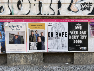 Multiple posters for concerts and events are wheat pasted to a wall. A poster for On Rape is visible in the middle, with the black text superimposed over a white wedding dress.